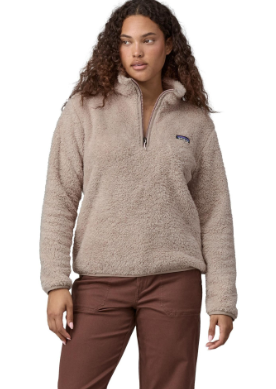 A woman modeling a beige sherpa fleece quarter-zip pullover with a small blue Patagonia logo on the left chest, paired with brown pants, against a plain white background.