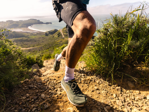 topo mens pursuit 2 shoe in the color green orange, a model wearing them while out trail running