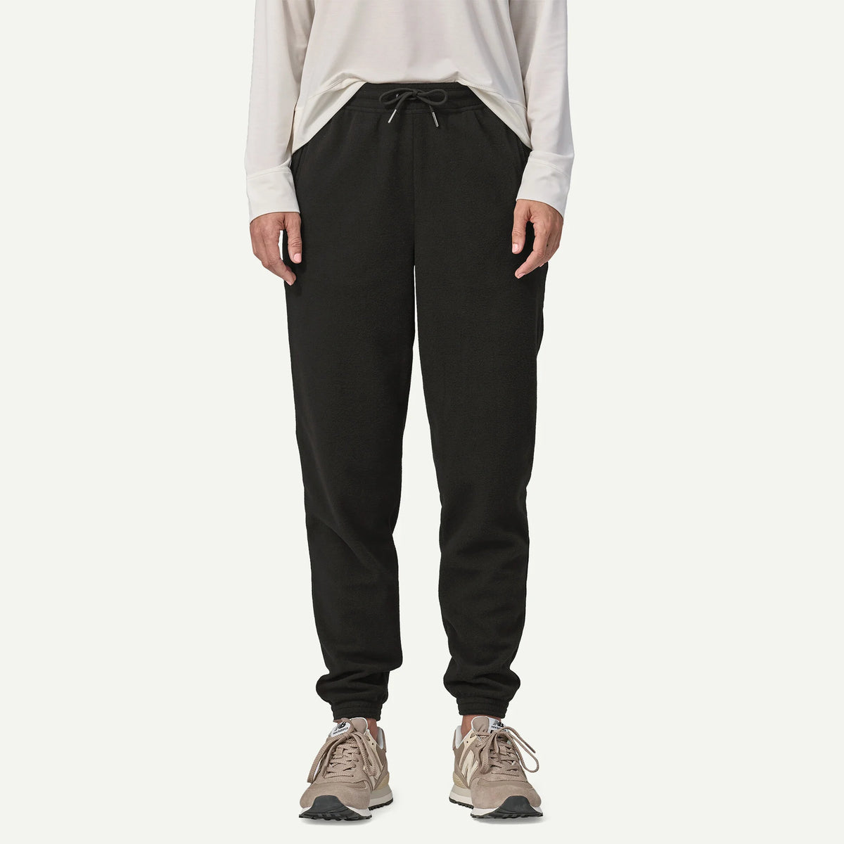 A person wearing black jogger-style pants with a drawstring waist, paired with a light long-sleeve top and beige sneakers, shown against a plain light background.