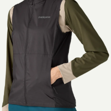 A close-up of a person wearing a dark gray zip-front vest over an olive green and beige long-sleeve shirt, with a small Patagonia logo visible on the chest.