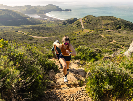 the topo womens pursuit 2 shoe in color grey mint, a model wearing them on a trail by the ocean