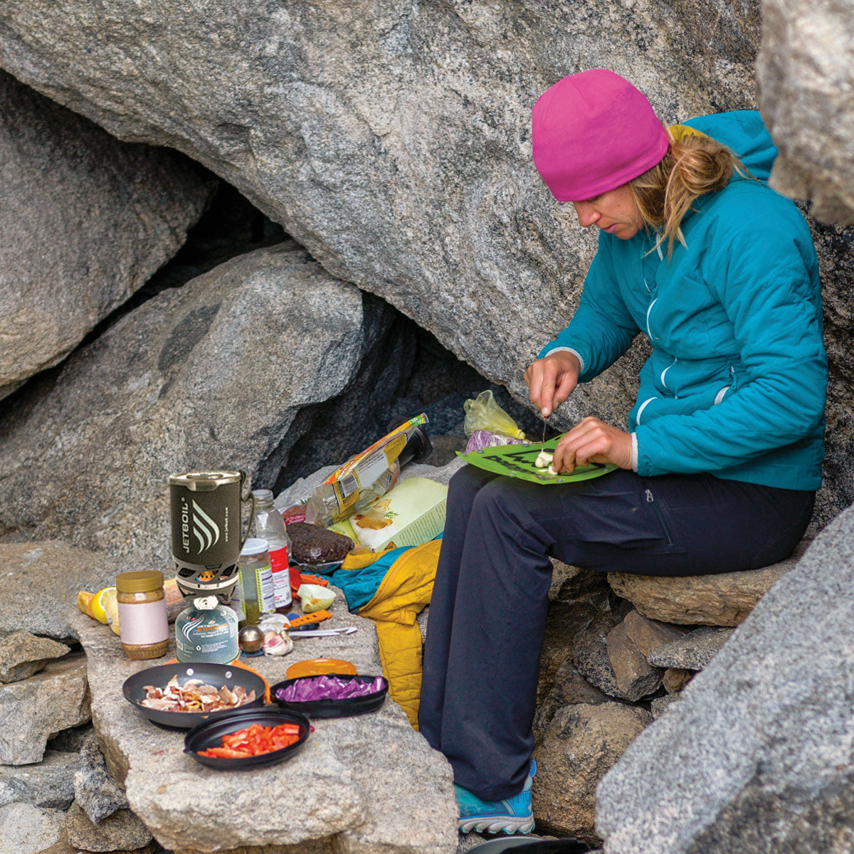 a woman prepares food in a rocky camp