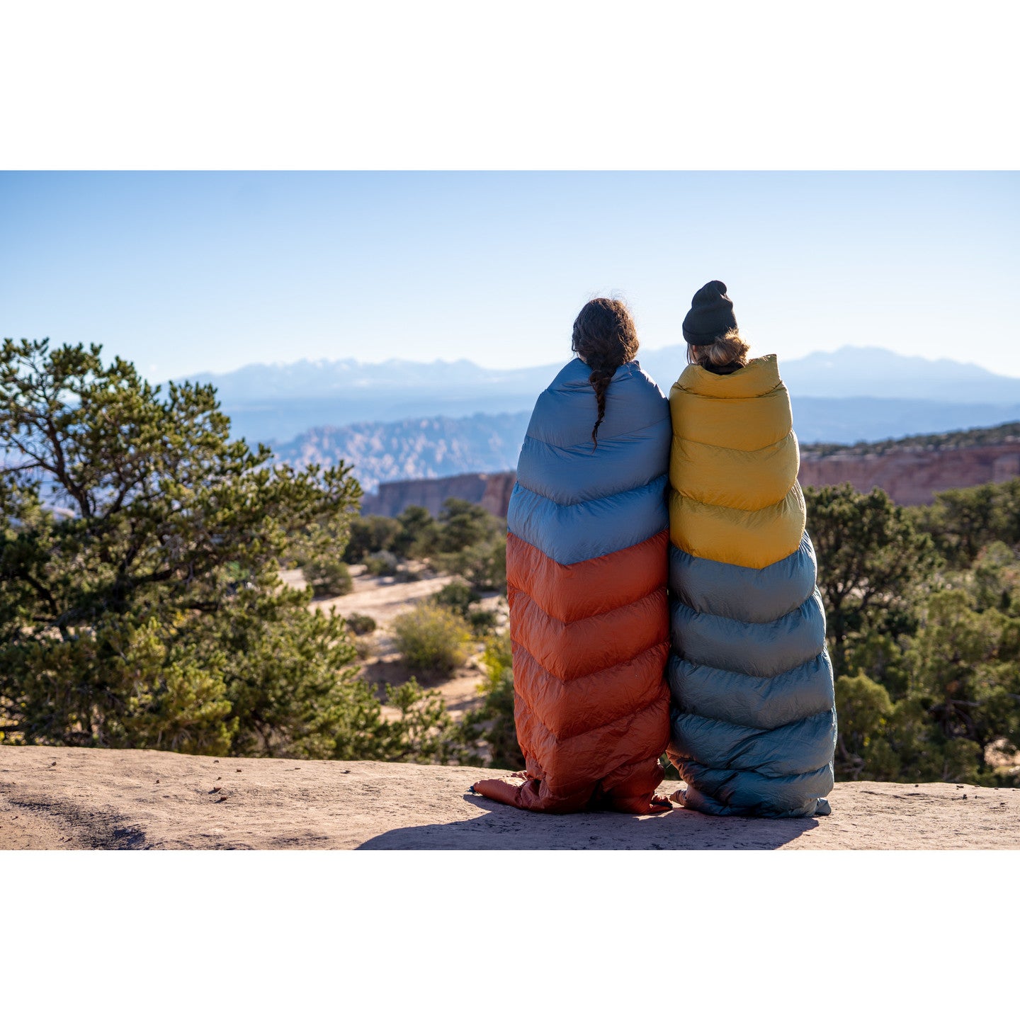 the kelty galactic 30 degree down sleeping bag. two models with the bags draped over them looking at the desert