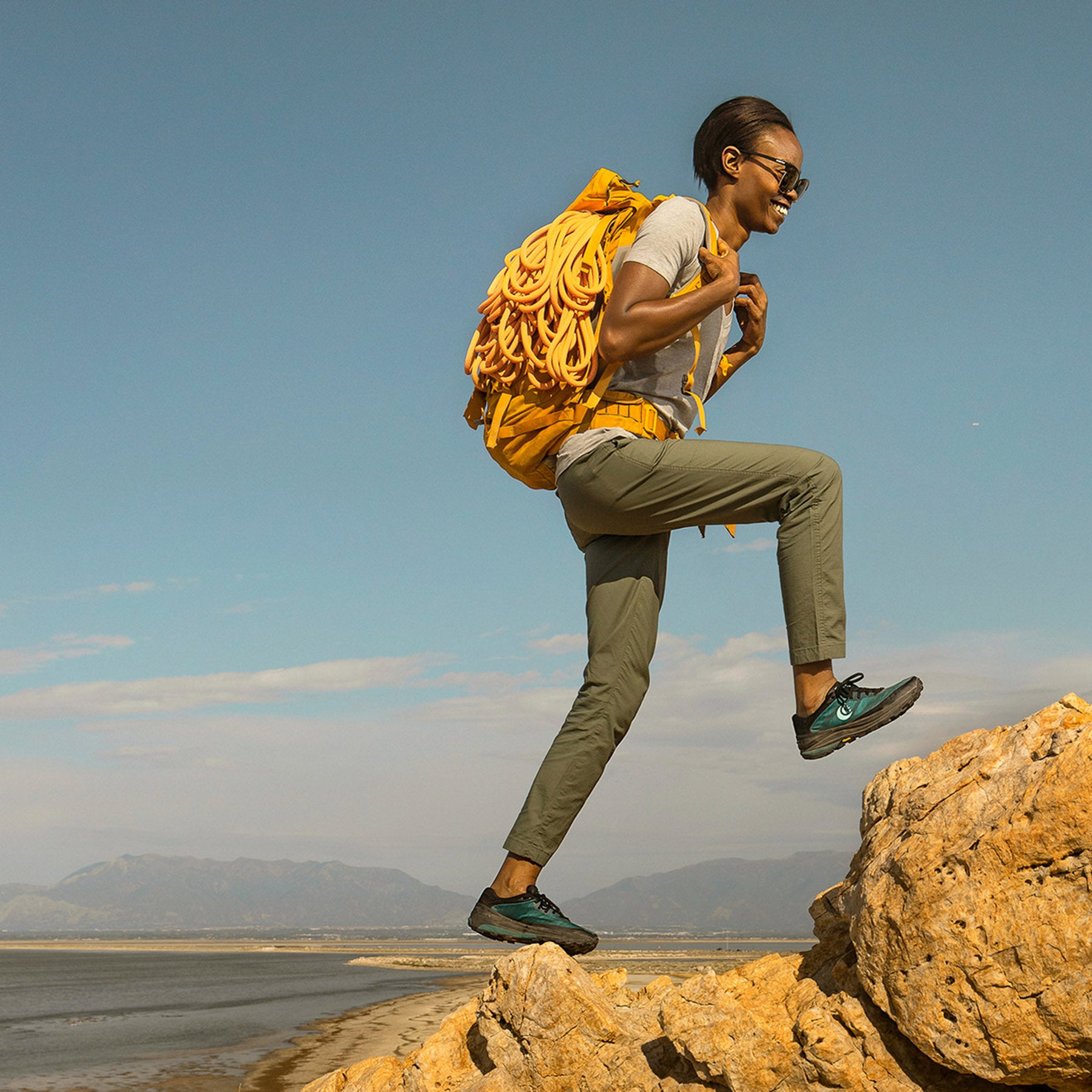 a model carries a backpack with an orange rope while hiking up some rocks in the Ultraventure pro