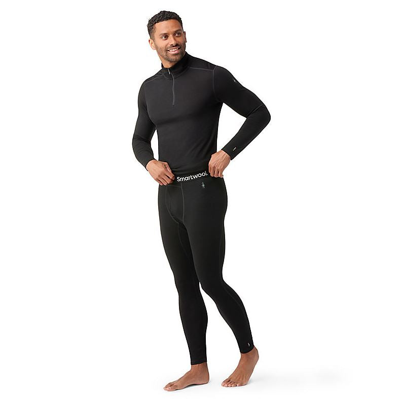 a photo of the smartwool men's classic all-season merino base layer bottom in the color black, front view on a model